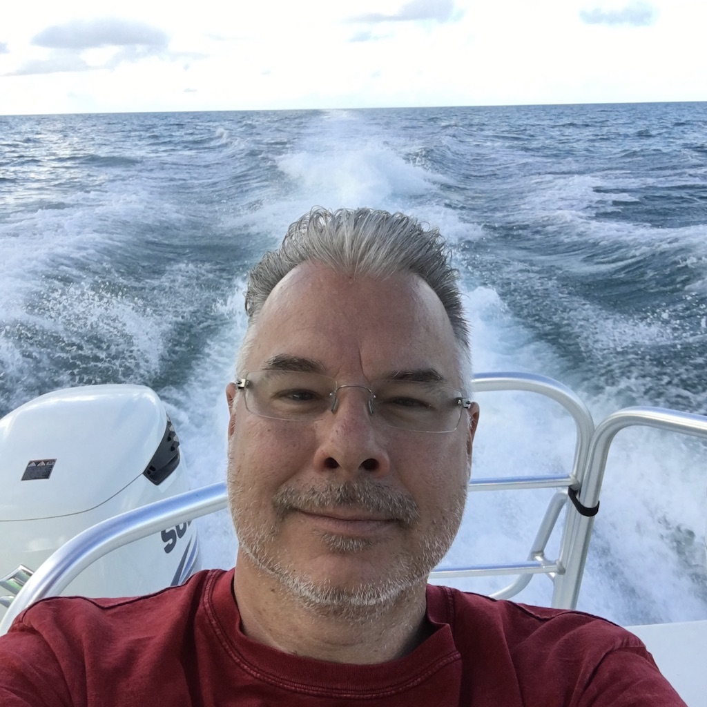 Mark sitting in the stern of a boat with the wake from teh engine behind him.
